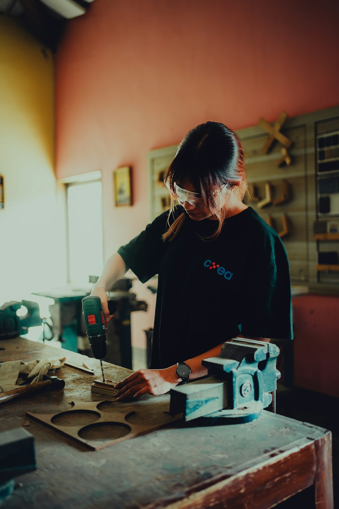 Woman operating a power drill on a wooden workbench.