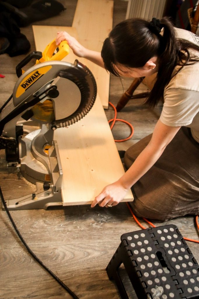 Woman carefully uses a miter saw on a wooden board.
